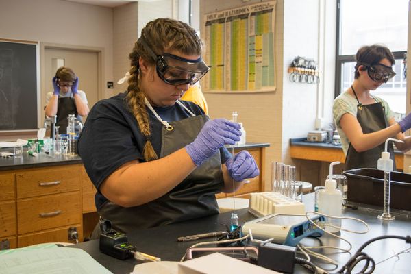 girl in braids in lab wearing purple gloves, goggles