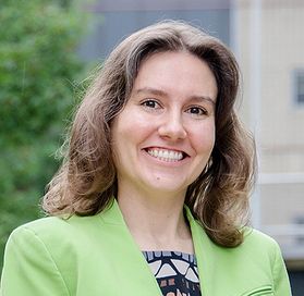 Headshot of WVU faculty Maggie Bennewitz. She is pictured outside wearing a lime green jacket over a patterned blouse. She has shoulder length light brown hair. 