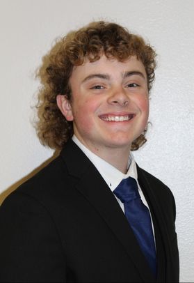A portrait of Connor Dorsey who is wearing a black jacket and blue tie against a white background.