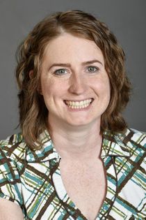 Headshot of woman smiling with brown hair and green and brown plaid shirt