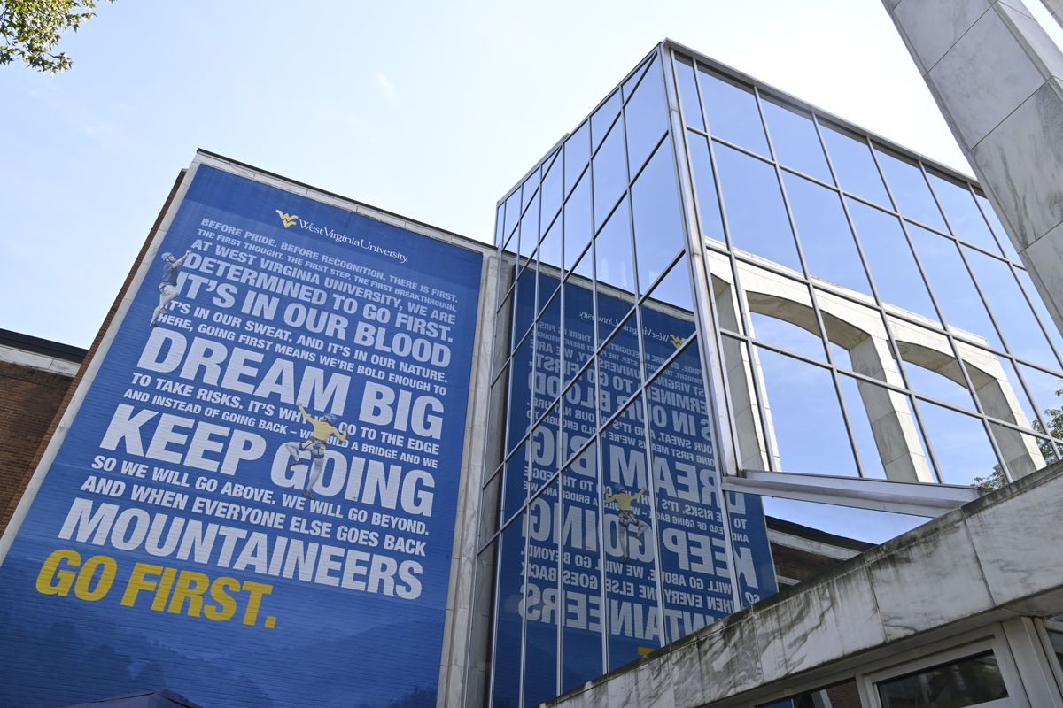 Perspective shot of the Mountainlair, the student hub for West Virginia University. The image captures the mountaineers go first mural, as well as the mirrored panels reflecting the clear sky.