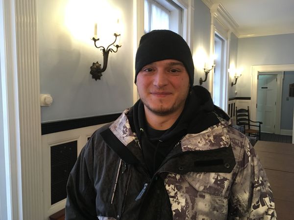 Man in two-toned jacket and black beanie smiles for a picture.