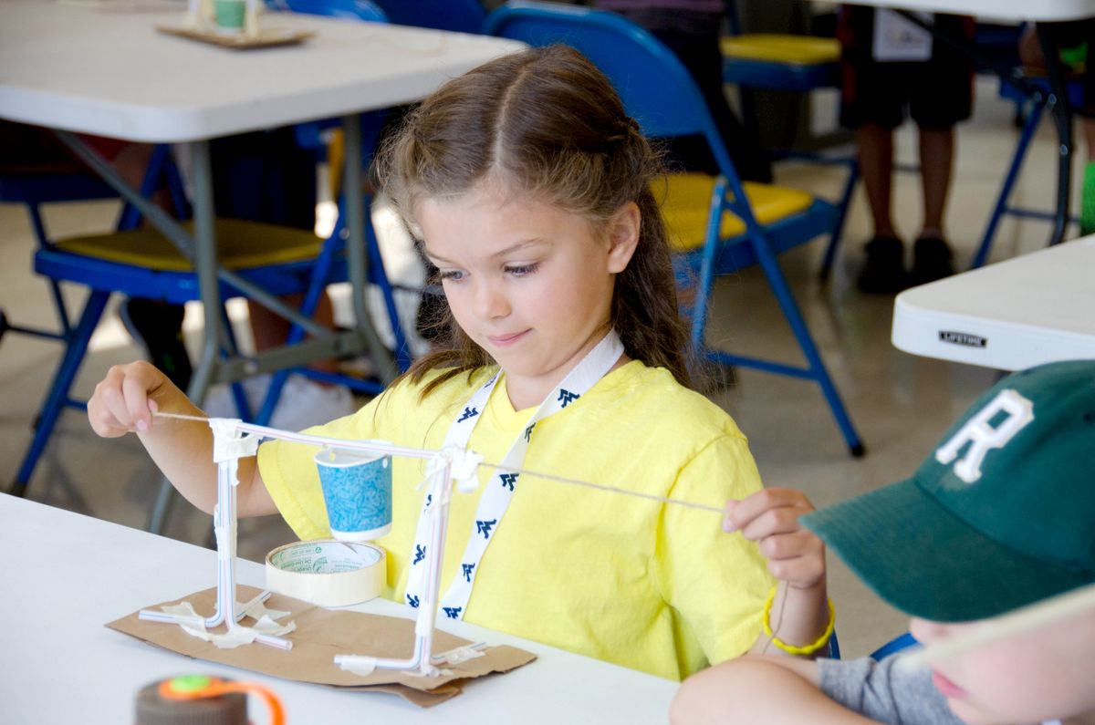 A little girl with brown hair and dressed in a yellow shirt works on a project at a previous WVU engineering summer camp. 