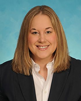 Headshot of WVU researcher Lisa Costello. She is pictured against a light blue background and is wearing a dark colored jacket over a white button-up shirt. She has shoulder-length blonde hair. 