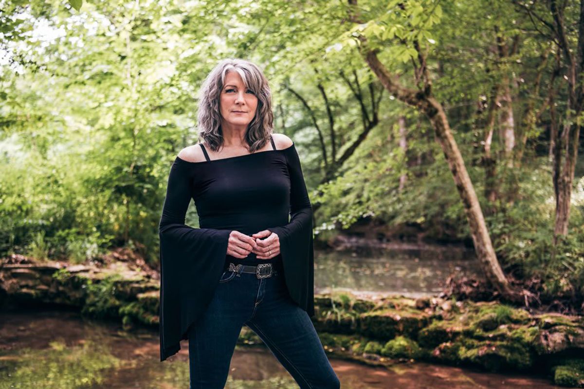 photo of woman in black top standing next to stream with trees in background