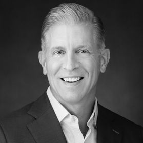 Headshot of new WVU Alumni Association Board of Directors member Michael Bell. The photo is black and white, and features Bell dressed in a dark sport coat over a white dress shirt. He has short, combed back hair. 