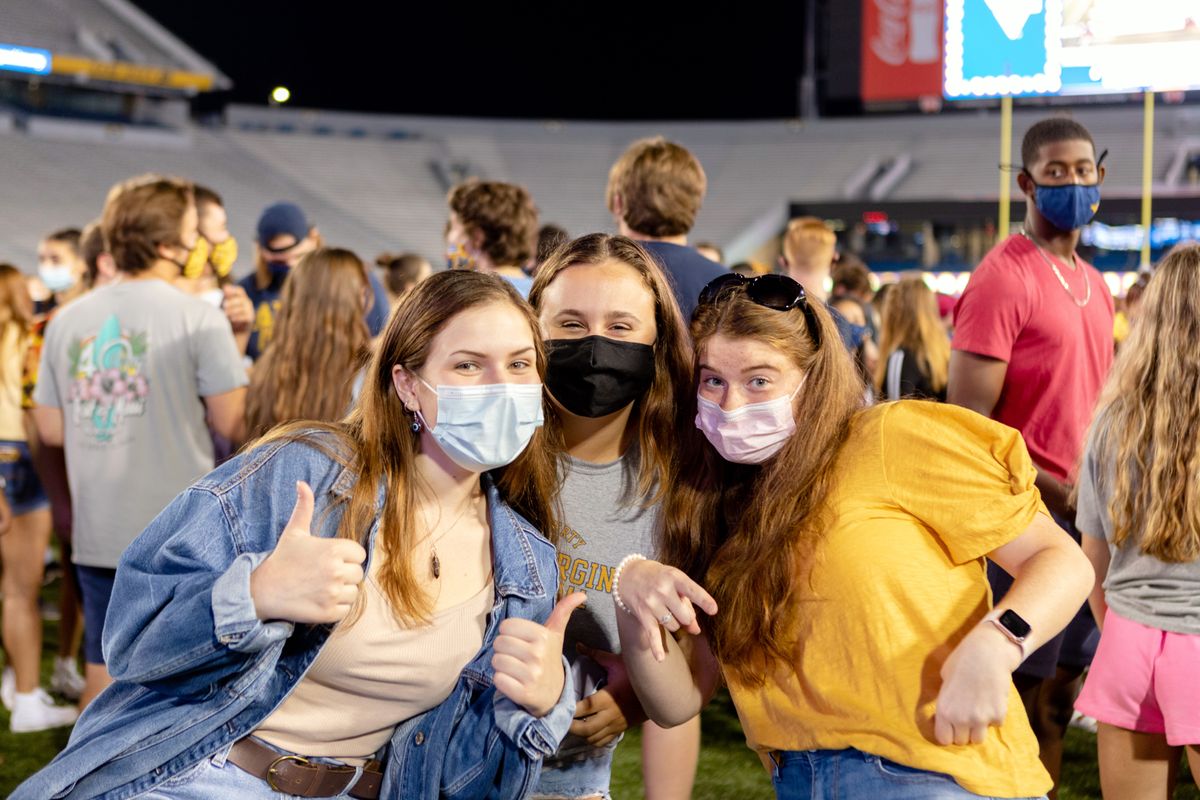Three girls wearing masks stand on the football field and pose for a picture.