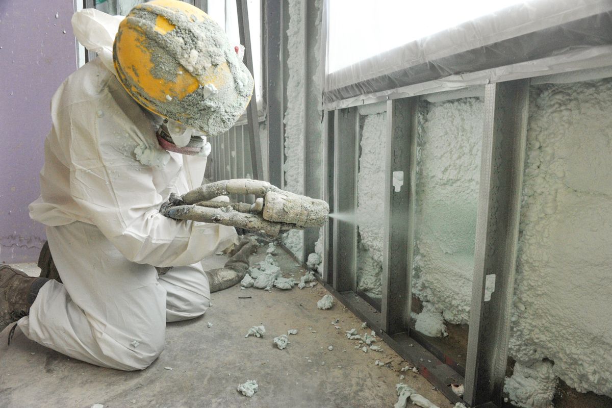 person in hardhat, white coveralls, sprays insulation in exposed walls