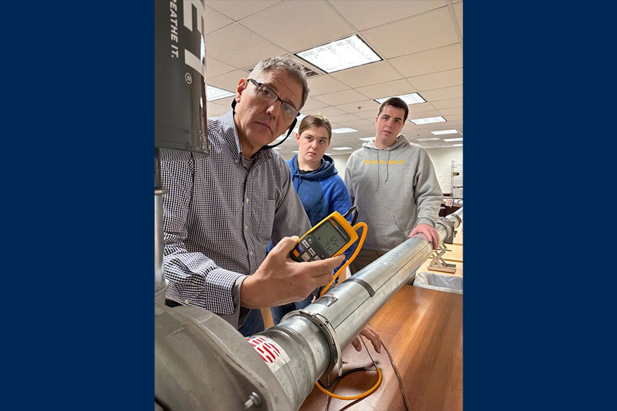 Photo featuring WVU professor Sergio Caporali-Filho in his industrial hygiene lab with two students, one male and one female. They are working with testing equipment and the professor is holding a controller. 