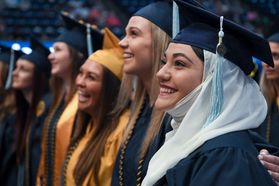 women smile while joining arms while wearing caps and gowns during a graduation ceremony