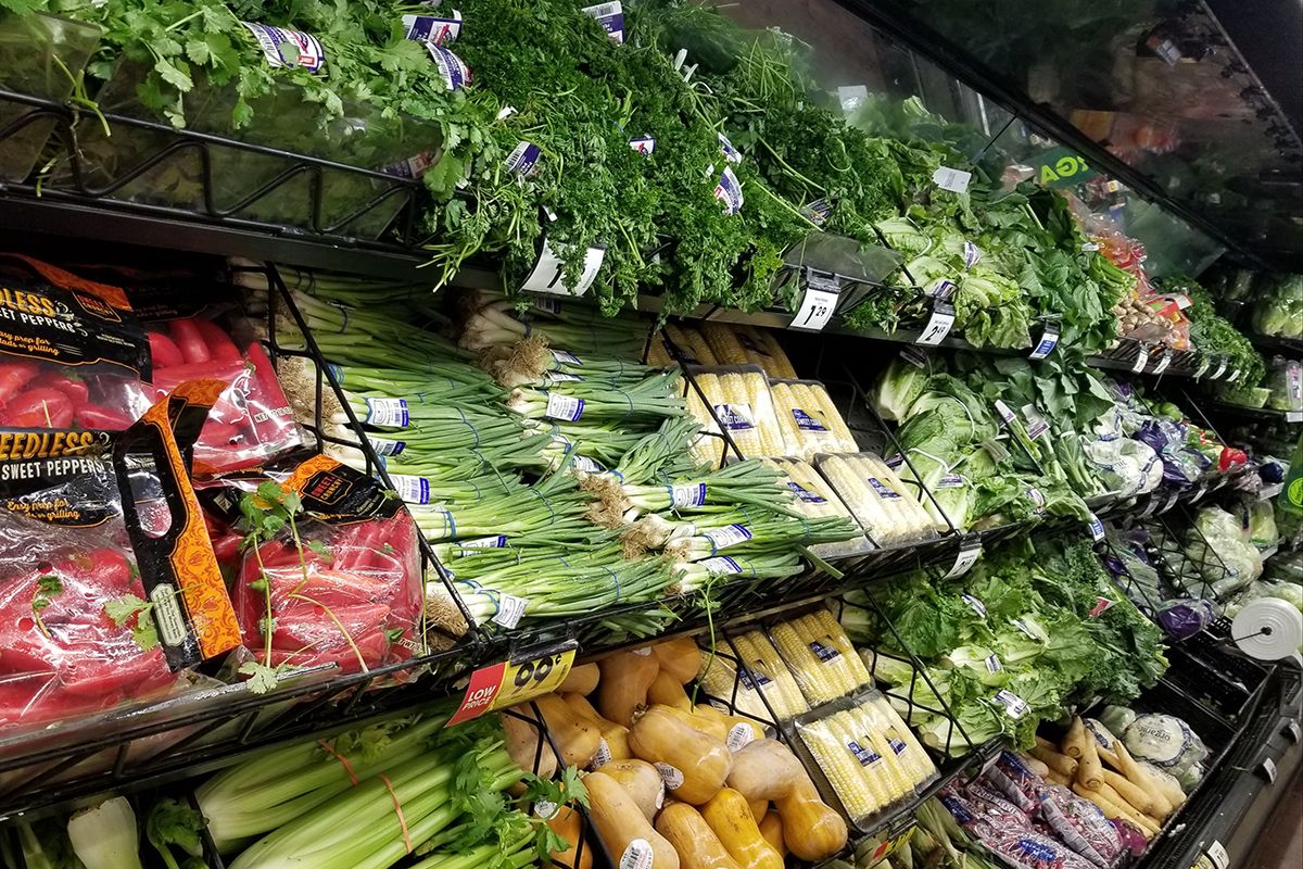 This is a grocery aisle of produce with green onions, wrapped corn, parsley, butternut squash and other loose vegetables visible.