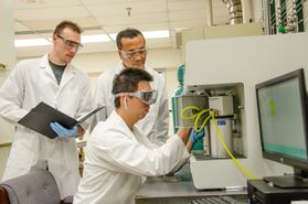 Three men work in lab coats and goggles