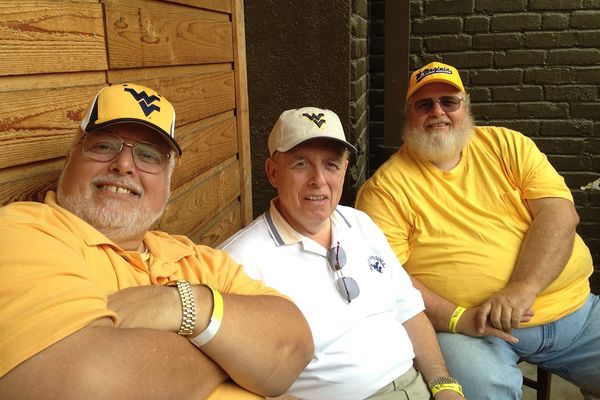 Three men wearing hats with a WVU logo and gold and white t-shirts smiling