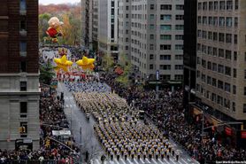 The Mountaineer Marching Band is shown in full formation marching down a street in New York City between tall buildings.