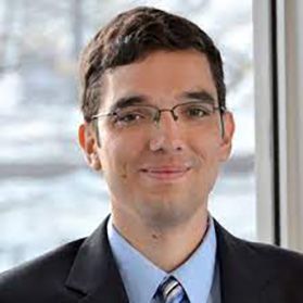 Headshot of WVU researcher Fernando Lima. He is pictured in front of a window wearing a dark suit over a light blue shirt and striped tie. He has short brown hair and wears glasses. 