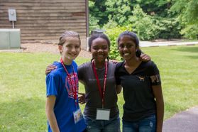 Three smiling girls join arms at 4-H camp.
