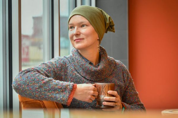 A woman with a mug wearing a scarf to cover her head looks out a window