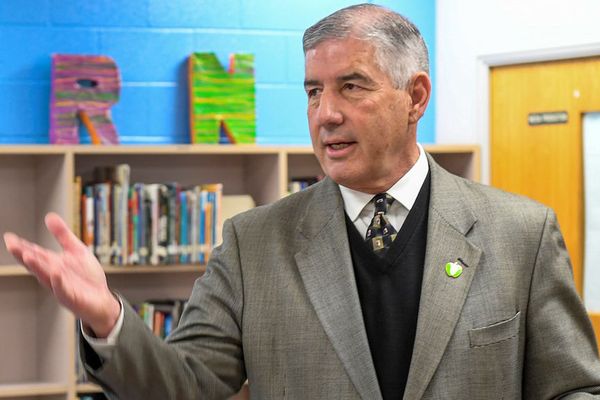 man with grey hair in a suit jacket and sweater gestures with his hand in a classroom