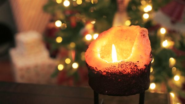 Close-up of a lit candle in front of a Christmas tree.