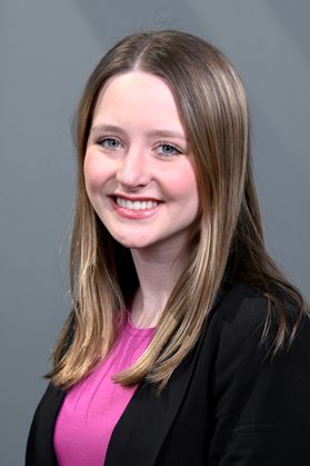 Headshot of WVU Foundation Scholar Jayla Boyd. She is pictured against a gray background wearing a black jacket and a pink blouse. She has long, dark blonde hair.  