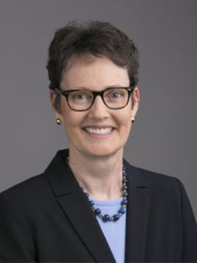 photo of smiling woman with short dark hair, glasses, wearing a lavender top and dark jacket