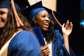 A graduate celebrates during the School of Public Health ceremony. The graduate is wearing a blue cap and gown and is shown waving.