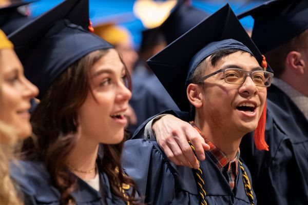 WVU students graduating wearing their navy blue caps and gowns with their arms wrapped around each other.