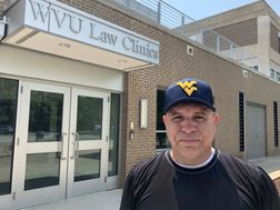 Man wearing grey shirt and blue hat with WV logo outside of the WVU Law Clinics