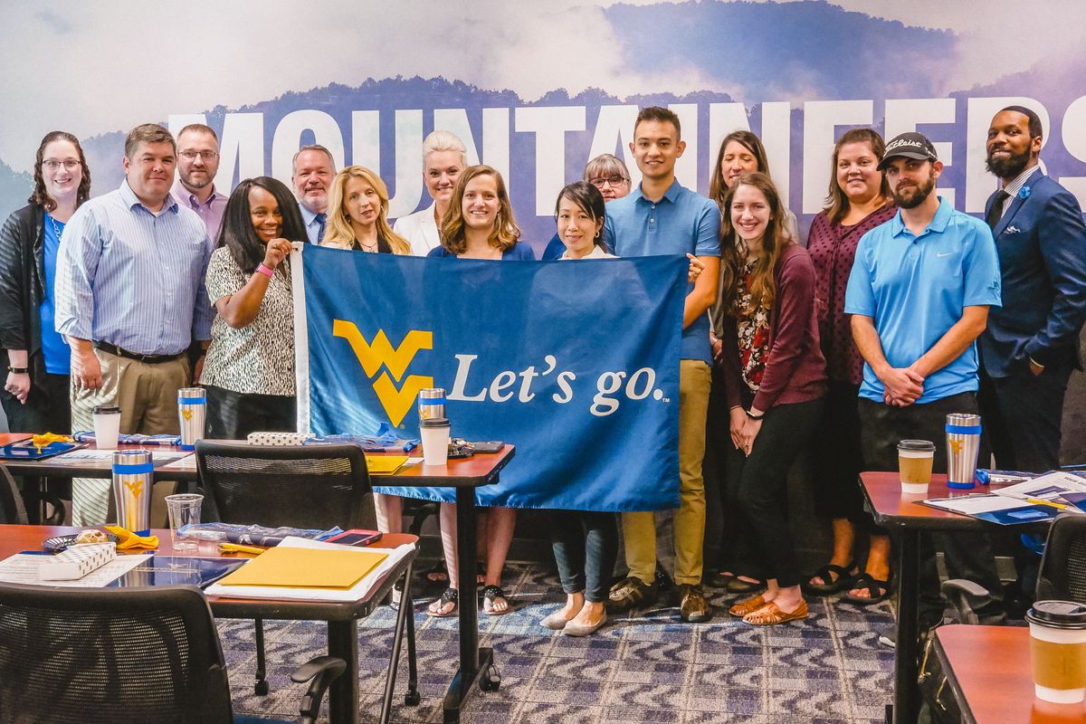 16 people stand in front of a Mountaineers sign while holding a blue 