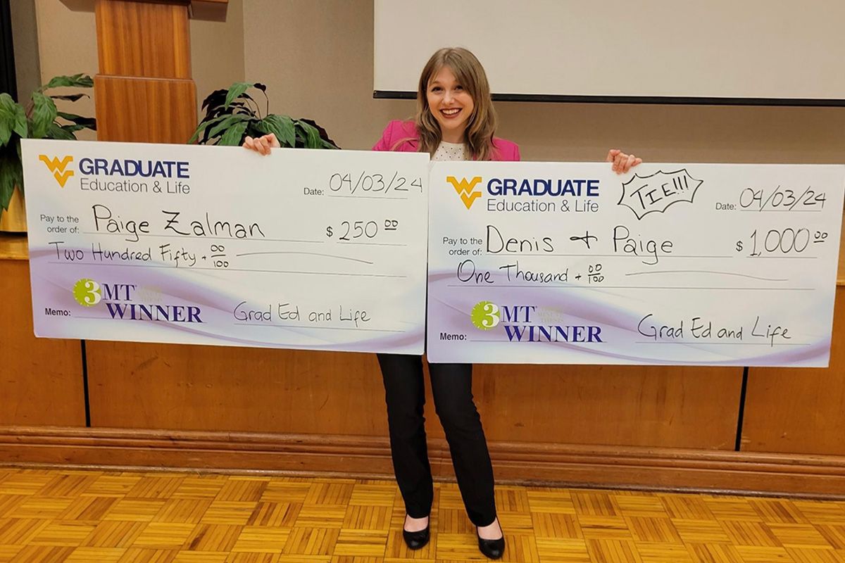 Photo of WVU gradate student Paige Zalman holding two giant checks for competitions that she won. 