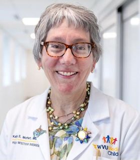 A woman with gray hair and glasses wearing a white lab jacket
