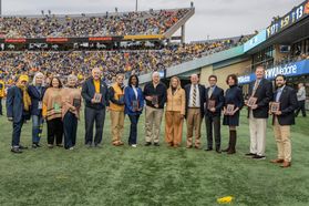 A group of WVU Homecoming award honorees pose on the field together during halftime of the football game. 
