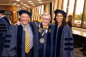 President Gordon Gee stands with his arms around Chambers College honorary degree recipients, Richard Adams and Diana Lewis Jackson. They are all in dark blue academic regalia.