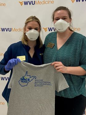 Two women wearing masks holding a t-shirt