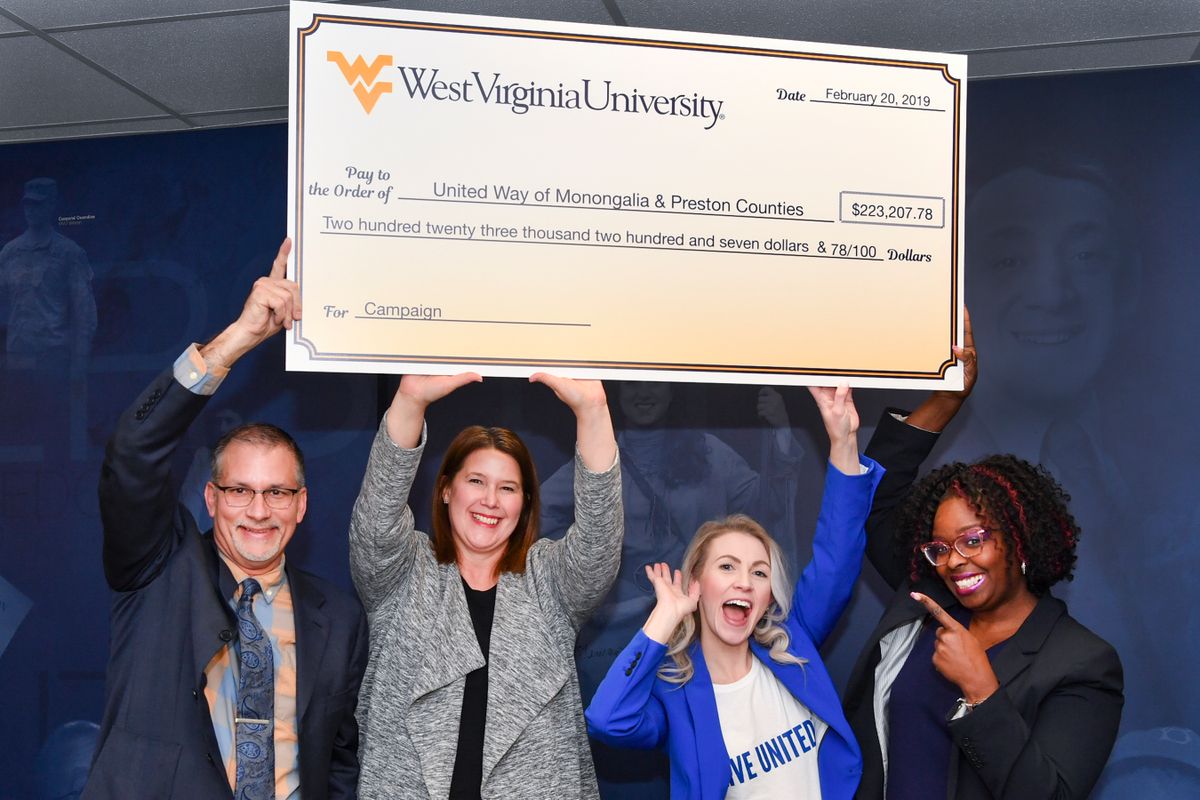 Four people hold a large check over their heads in celebration