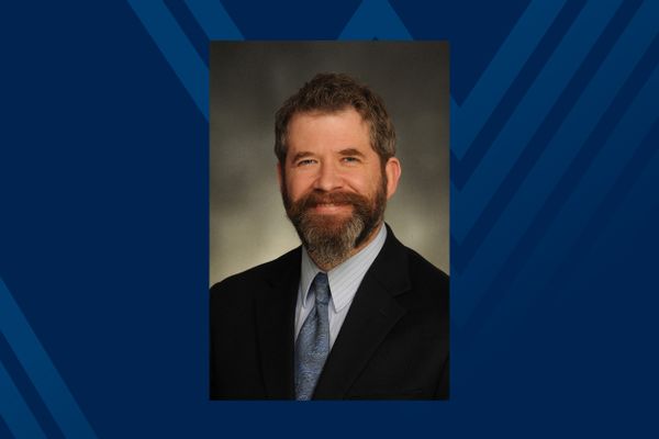 photo of smiling man with beard in suit and tie on blue background