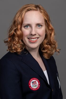 portrait of a young woman with reddish-blond hair wearing a dark jacket with a patch bearing the American flog and the Olympic rings