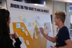 Photograph showing two WVU students adding post it notes to a board that says: "Where do you want to have an impact?"
