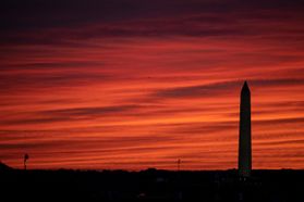The Washington Monument is cast in silhouette against an orange sky at sunset.