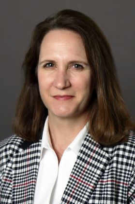 photo of barely smiling woman in black and white plaid blazer, white shirt
