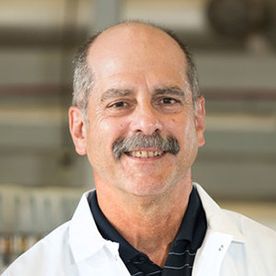 Headshot of WVU professor Paul Ziemkiewicz. He is wearing a white lab coat with a dark shirt underneath. He has a receding hairline and a gray mustache. 