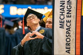 graduate in cap and gown smiles while making a heart with his hands