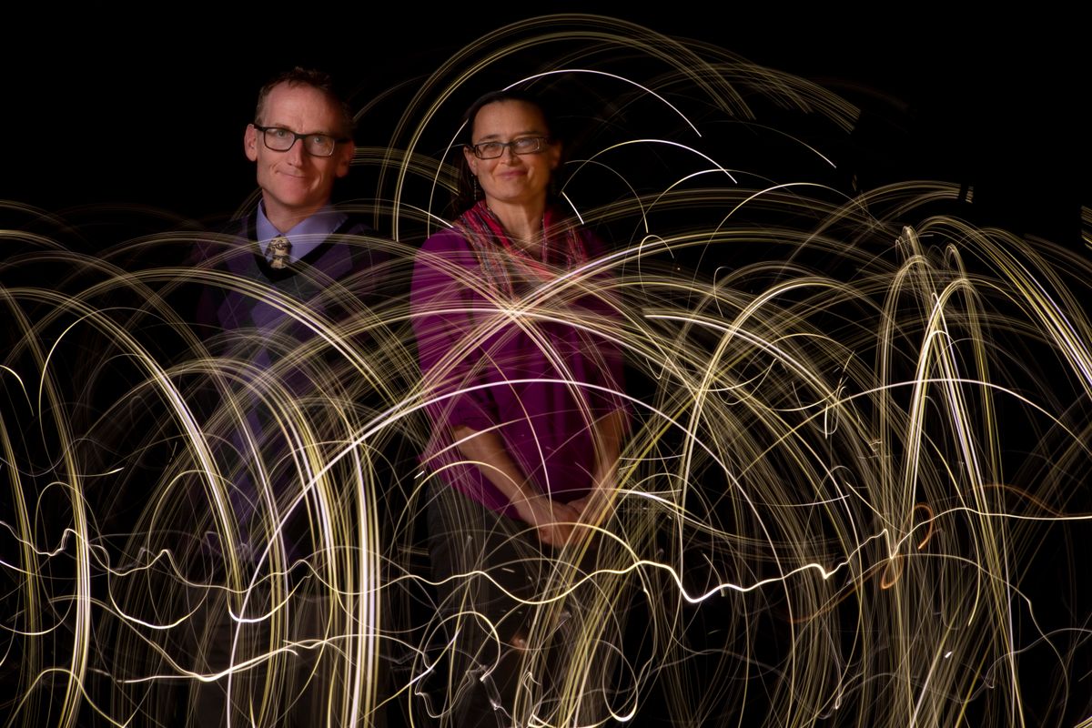 Duncan Lorimer and Maura McLaughlin pose together for a photograph against a black background with light waves in front of them. 