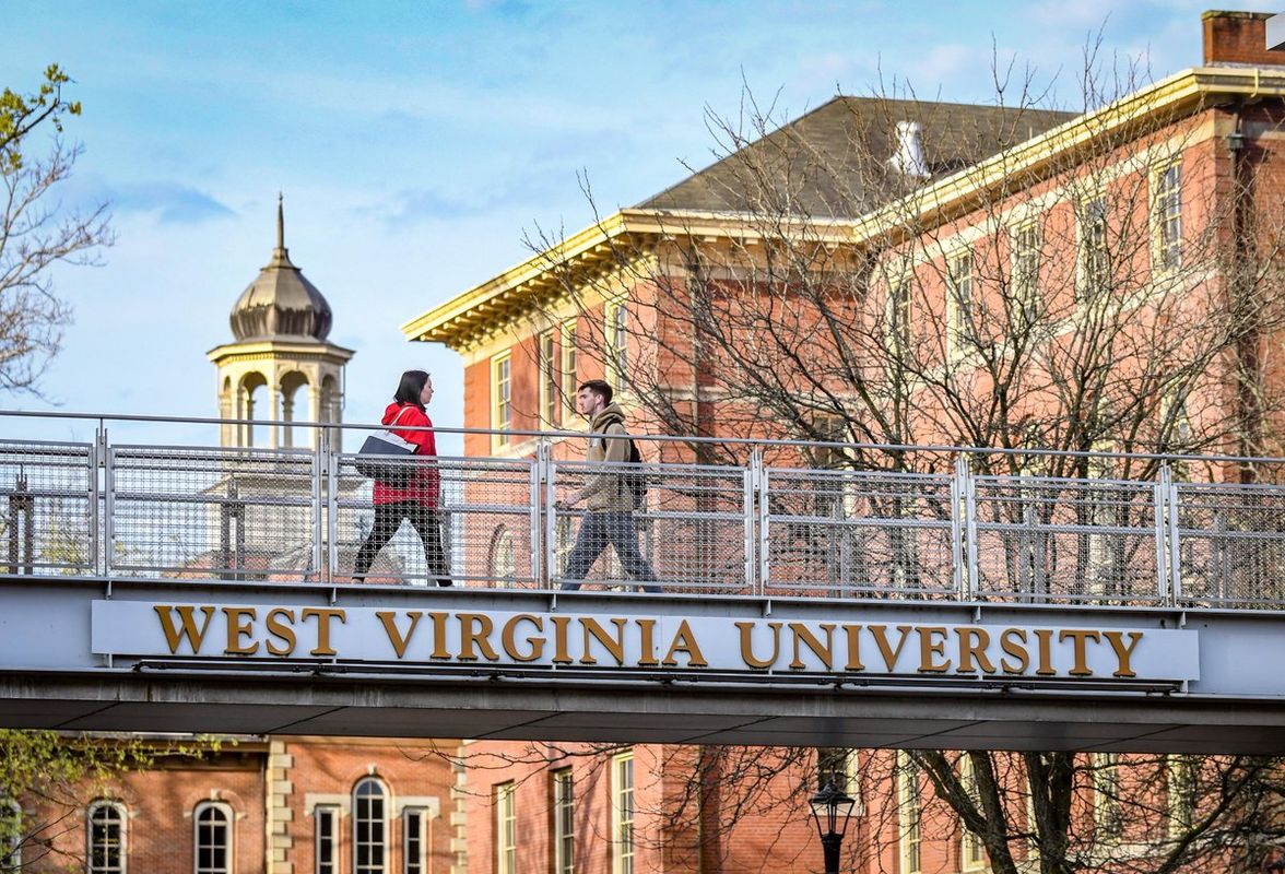 people walk across a footbridge with West Virginia University on the beam