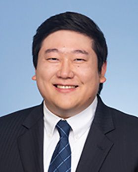 Headshot of WVU Cancer Institute doctor Stehen Yu. He is pictured against a light blue background wearing a dark jacket over a white dress shirt and blue plaid tie. He has short, black hair. 