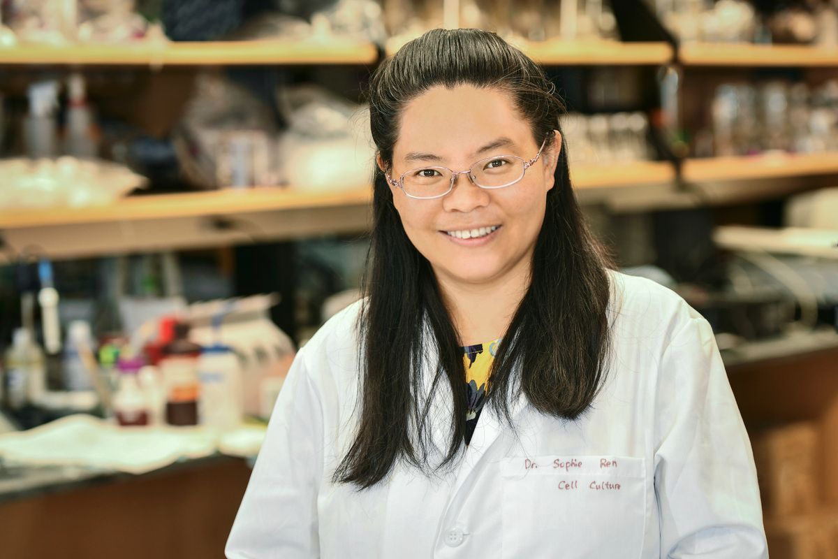 Smiling Asian woman in lab, wearing lab coat