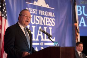 A man stands behind a podium with a West Virginia Business Hall of Fame banner in the background