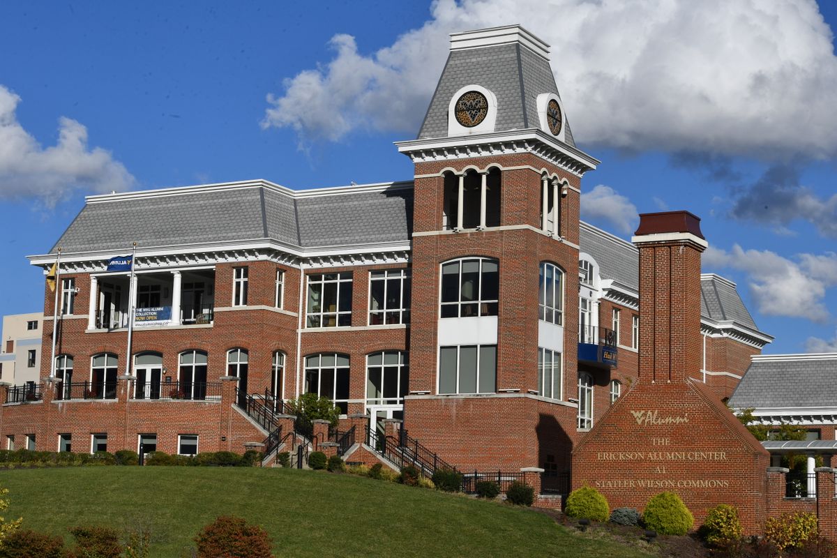 Photograph of the exterior of the Erickson Alumni Center on the Morgantown Campus at WVU. The red brick building stands tall agains a bright blue sky with puffy white clouds. 