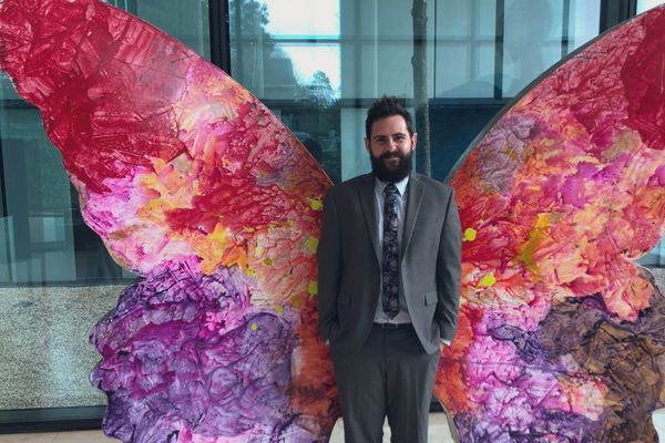 man stands in front of colorful insect wings sculpture