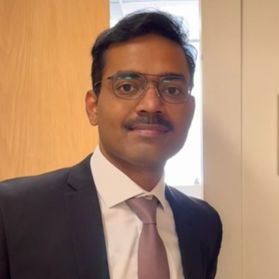 WVU researcher Sharan Bobbala. He is pictured inside standing in front of a wood-paneled wall and wearing a dark colored suit over a white dress shirt and mauve tie. He has short dark hair and a dark mustache, and wears glasses. 